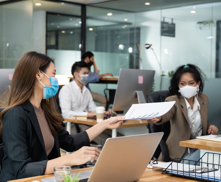Office workers pass a stack of papers while wearing masks.
