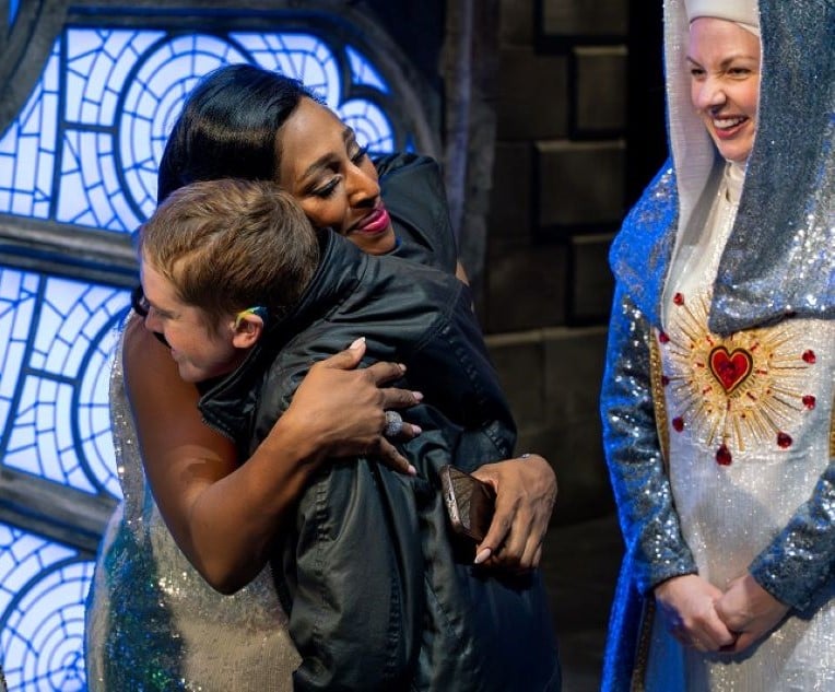 Performers hug on a theatre stage