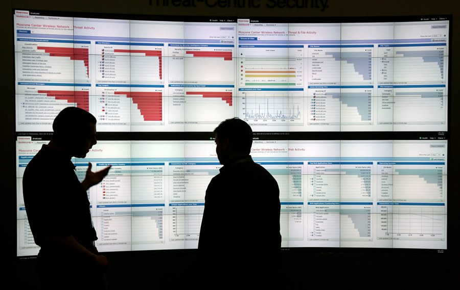 two men in front of large computer dashboard screens