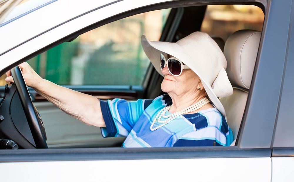 older woman in hat and sunglasses driving a car