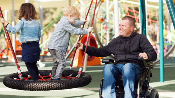 man in a wheelchair playing with kids on playground