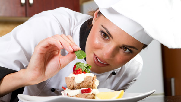 woman chef adding ingredients to food on plate