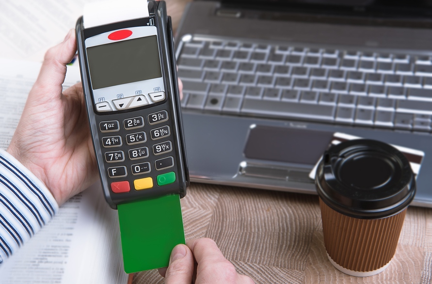 Credit-card-payment-terminal-man's-hand-with-laptop-crop-shutterstock_239126047-nata-lunata