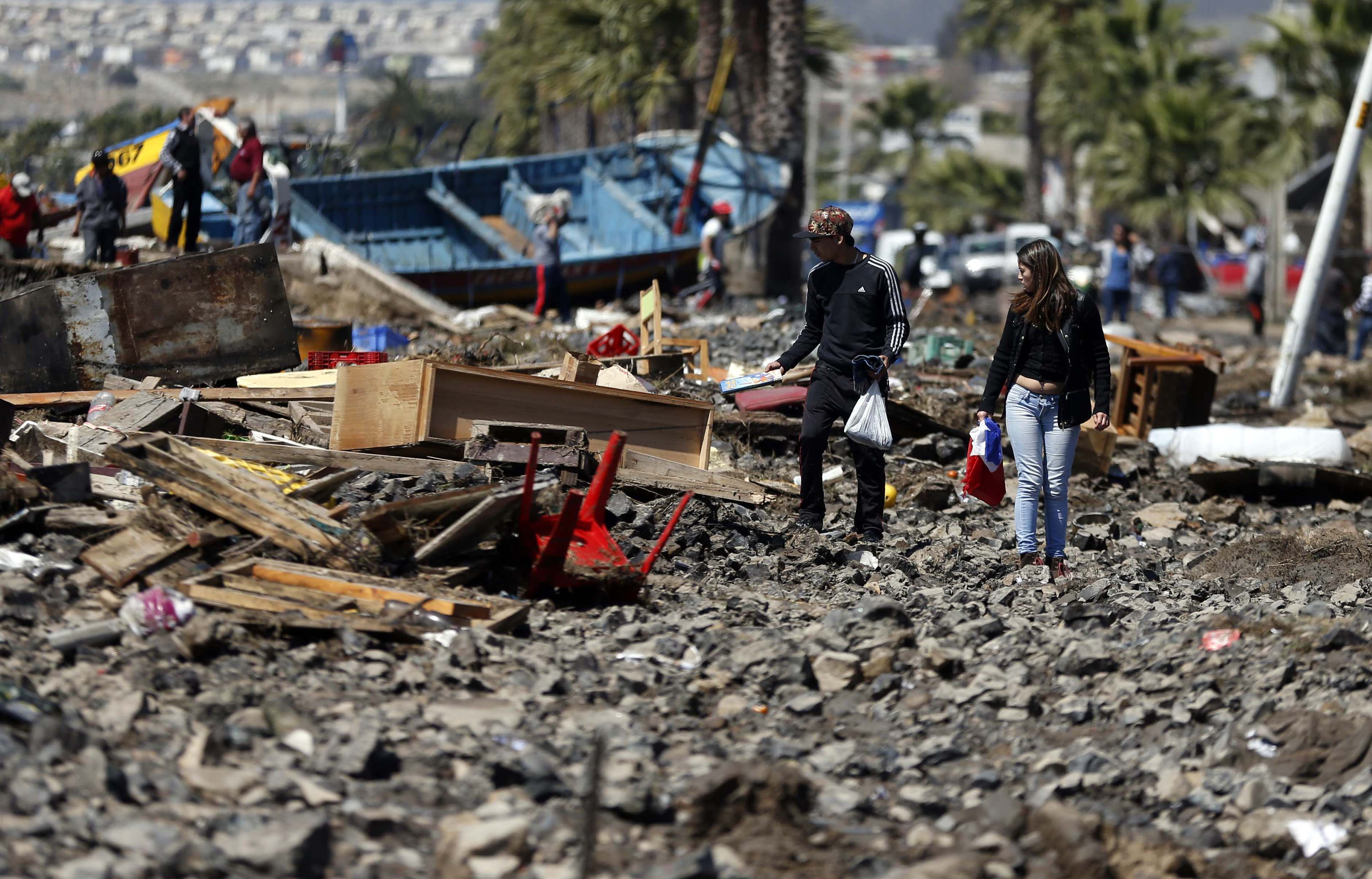 People walk through debris left behind by an earthquake-triggered tsunami in the coastal town of Coquimbo, Chile,