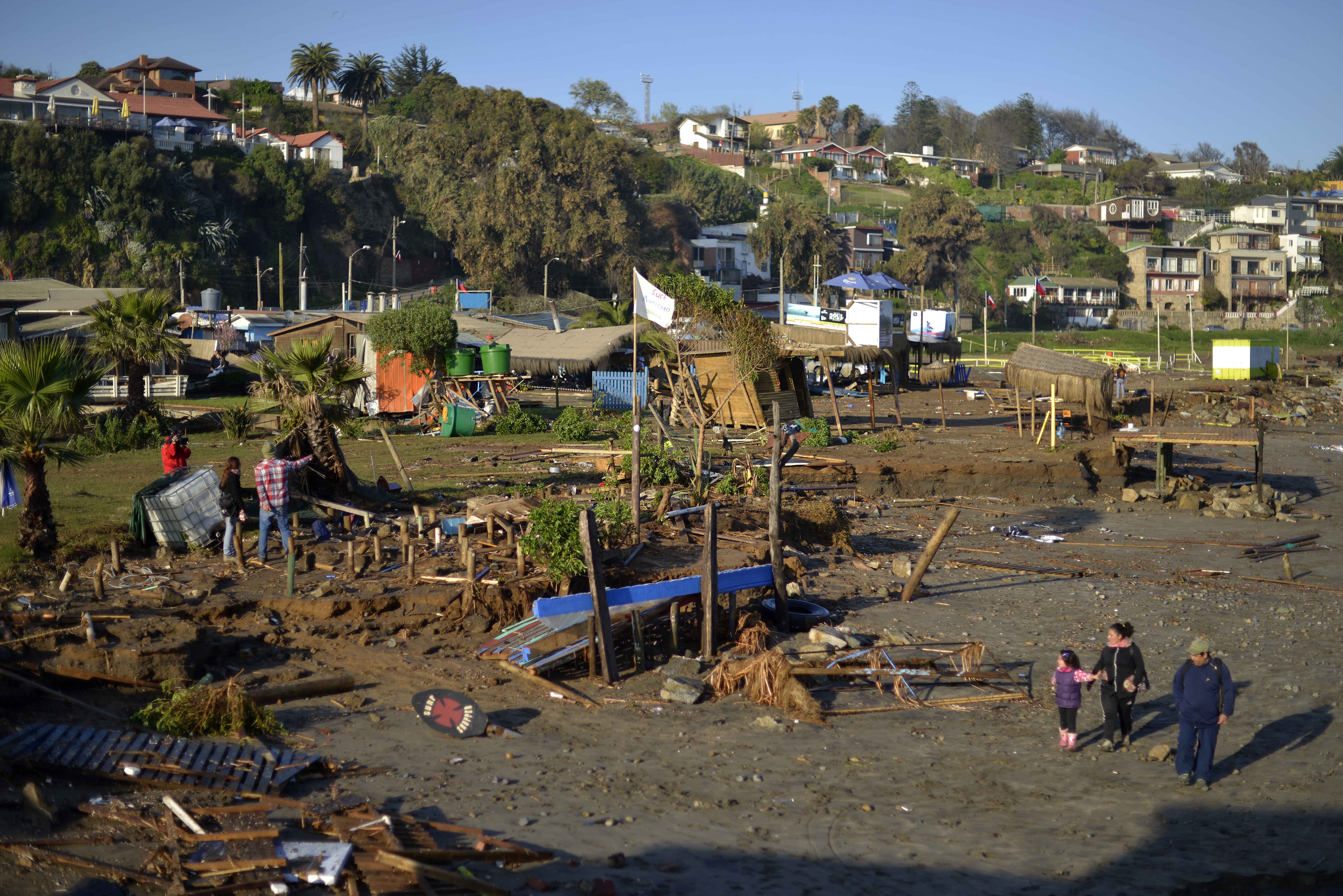 People walk past destroyed surfing schools on the beach after an earthquake-triggered tsunami in Concon, Chile