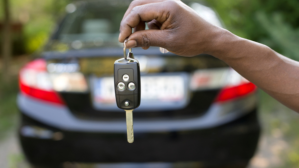 Hand-holding-car-keys-with-car-in-background-Shutterstock