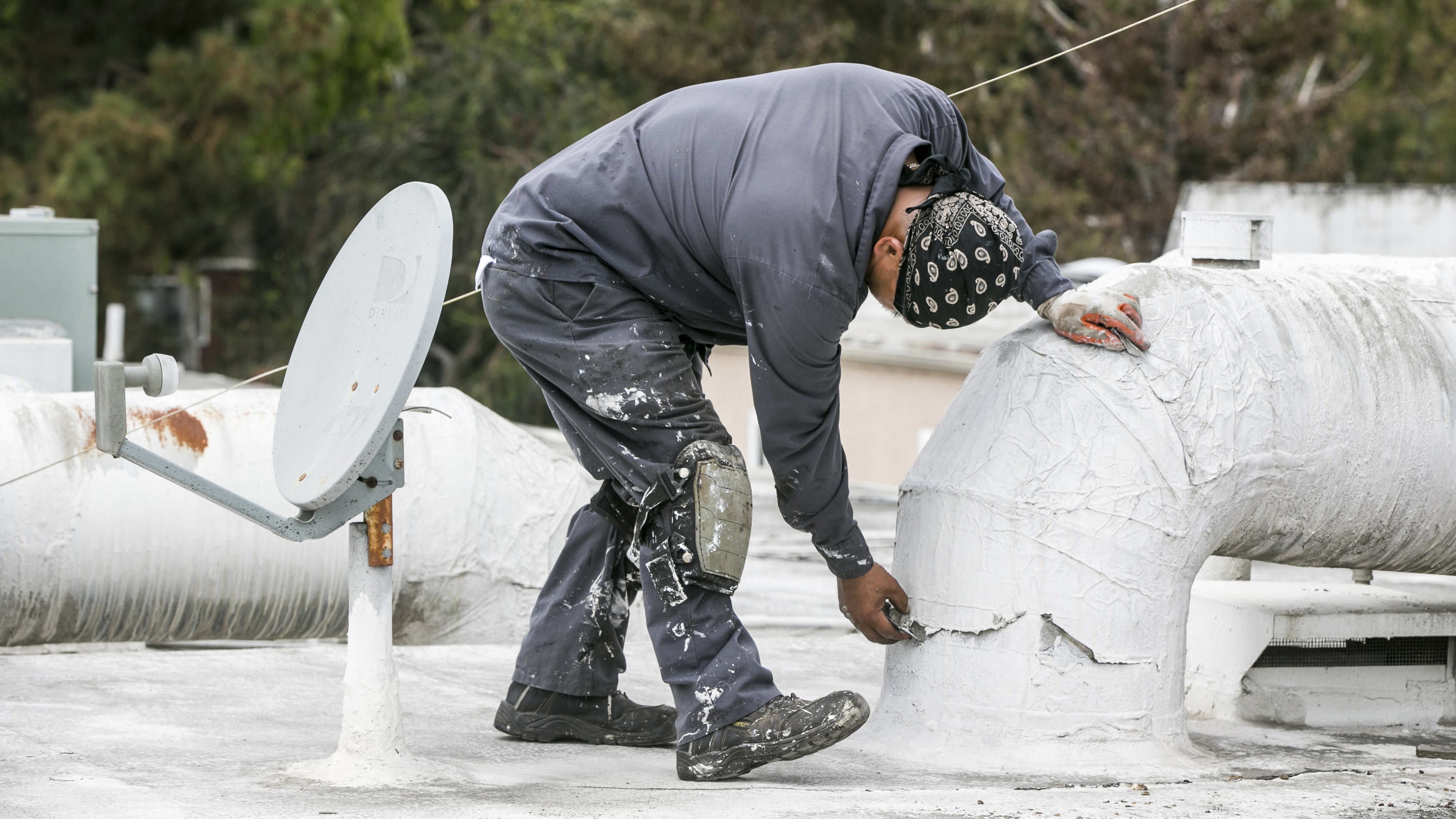 Roofer-inspecting-waterproofing-on-AC-duct-Calif_ElNino-crop-AP_809772792925-DamianDovarganes