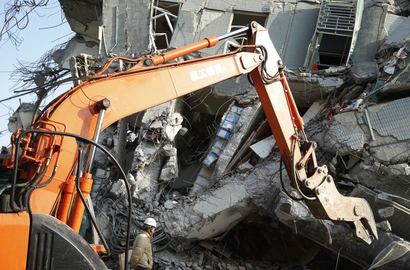 a rescue worker stands near tin cans exposed in the cement structure of the collapsed building