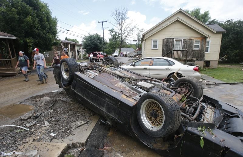 Overturned cars litter the street as residents clean up from severe flooding 