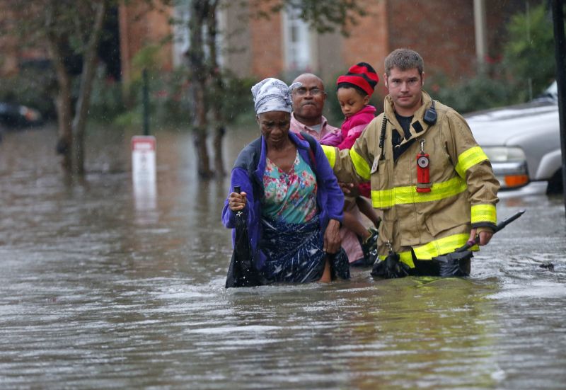 A member of the St. George Fire Department assists residents as they wade through floodwaters