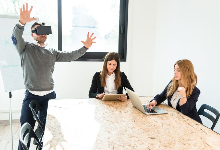 Man viewing virtual reality in conference room with 2 women