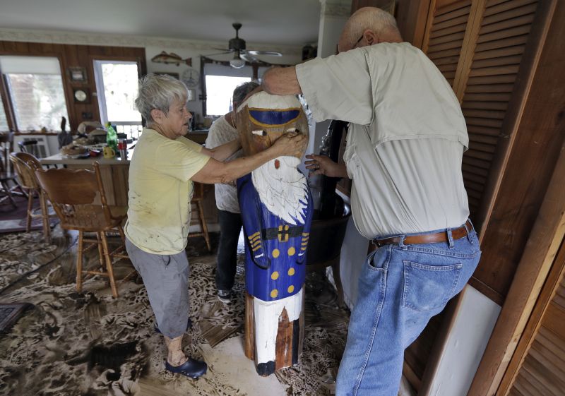 Bobbi Pattison, left, with help from her neighbors Hugh and Harriet Oglesby, stands up a sea captain statue