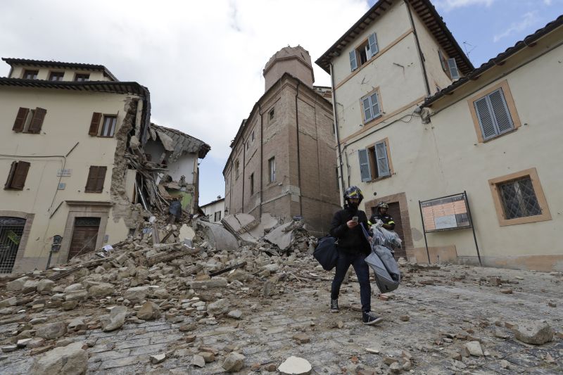 A resident carrying his belongings passes in front of the collapsed bell tower of the Santa Maria in Via church in the town of Camerino, Italy