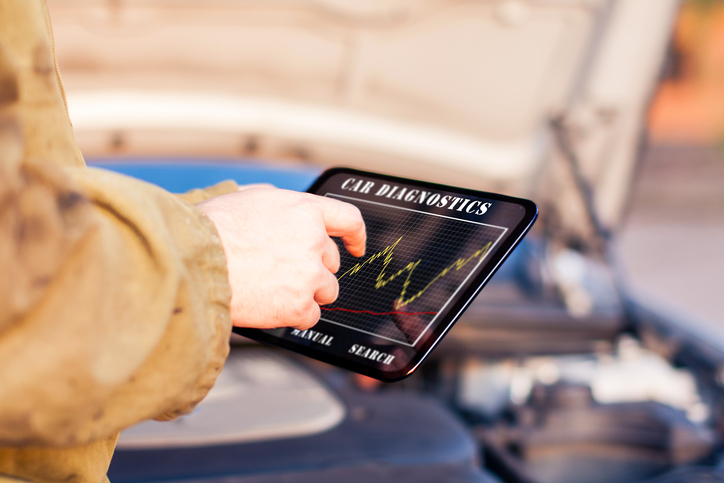 technician checks computer scan of car engine