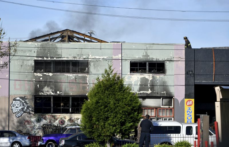 A firefighters walks on the roof of a smoldering building after a fire tore through a warehouse party 