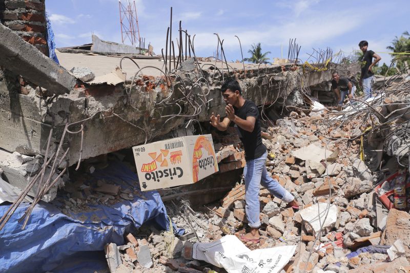 A man removes a box from under the rubble of a building that collapsed after an earthquake in Pidie Jaya, Aceh province, Indonesia