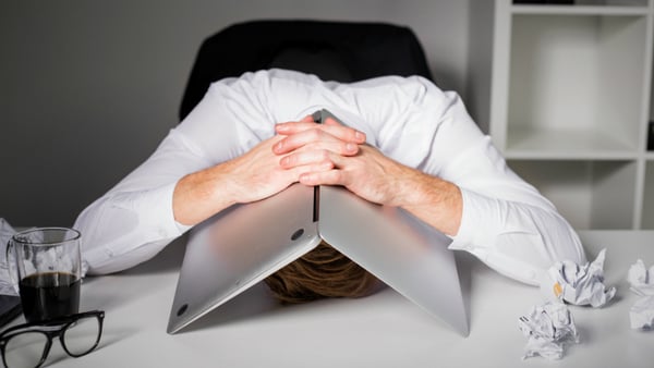 bad employee with head on desk under laptop