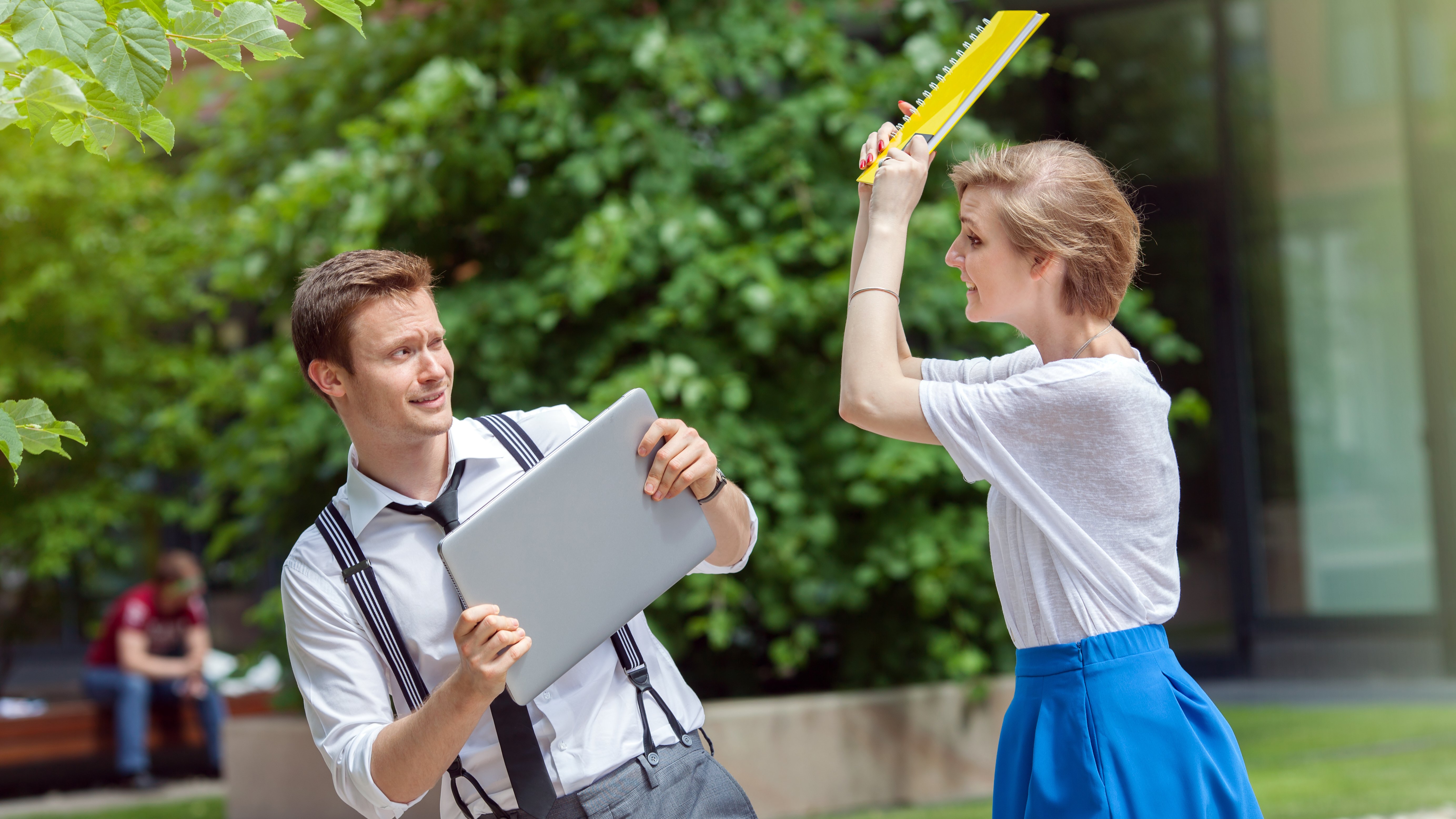 Woman hitting man with computer on the head with notebook