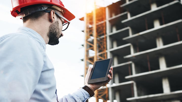 Young man in hard hat with handheld computer at construction site