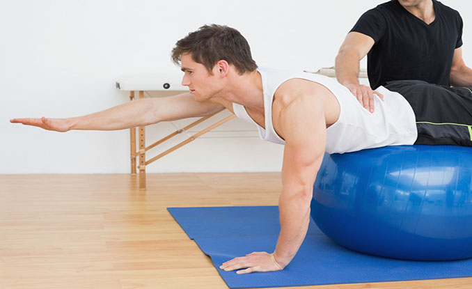 Physical therapist helping young man with yoga ball