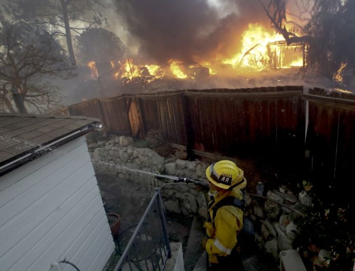 A Los Angeles County firefighter puts water on a burning roof during a wildfiA Los Angeles County firefighter puts water on a burning roof during a wildfire in the Lake View Terrace area of Los Angelesre in the Lake View Terrace area of Los Angeles