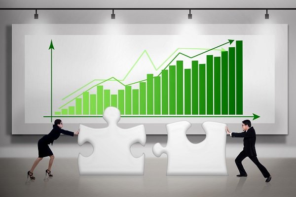 man and woman fitting puzzle together in front of green rising stock chart