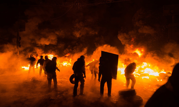 A group of protesters are silhouetted in front of a tire fire. 