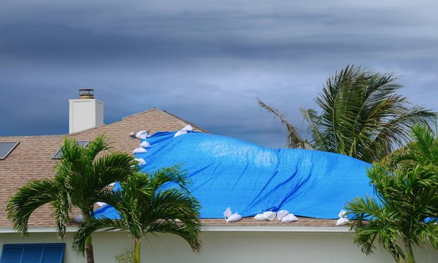 Storm damaged roof on house with a blue plastic tarp over hole in the shingles and rooftop. (Credit: Michael O'Keene/Adobe Stock)