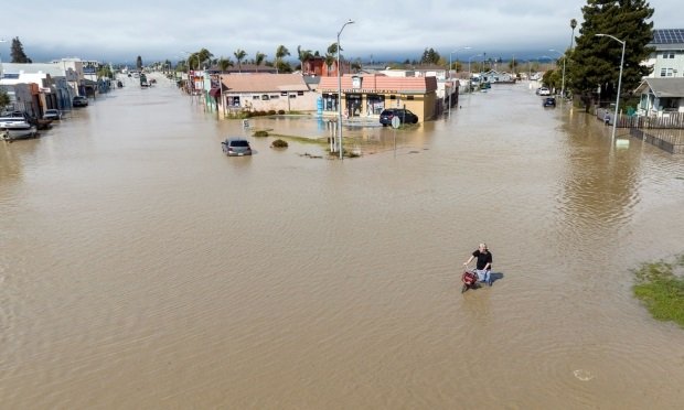 An aerial view shows a man navigating floodwaters with his bicycle in the unincorporated community of Pajaro in Watsonville, California, on March 11, 2023. (Credit: Josh Edelson/AFP/Getty Images)
