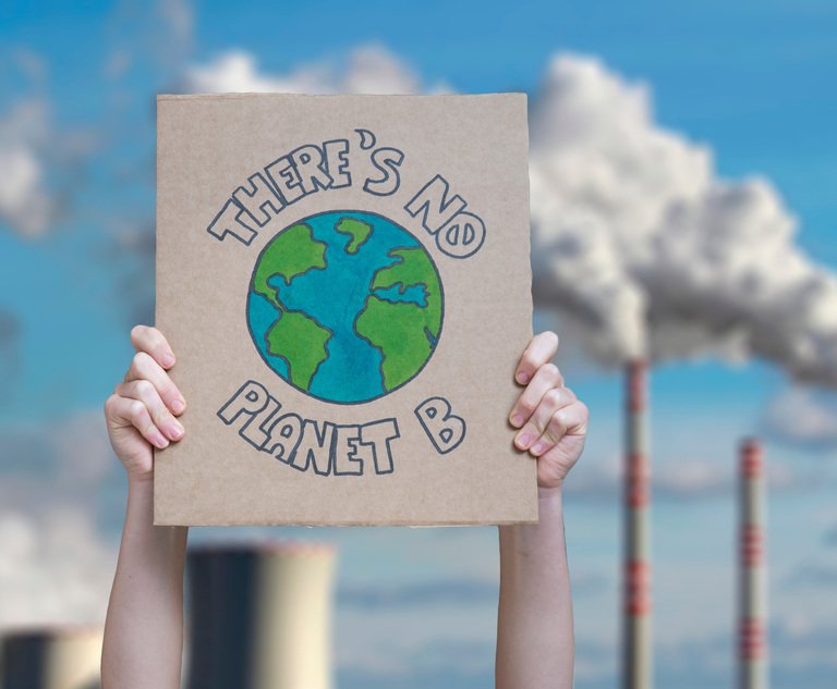 A person holding a sign that says "There is no planet B" in front of some smoke stacks.