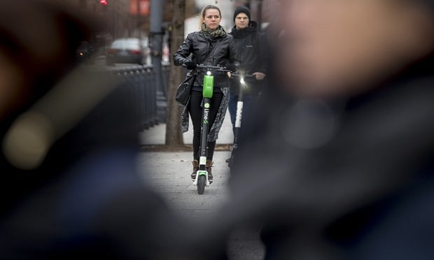 In this Dec. 4, 2018, photo a couple rides scooters near the White House in Washington. Electric scooters are overtaking station-based bicycles as the most popular form of shared transportation outside transit and cars. (AP Photo/Andrew Harnik)