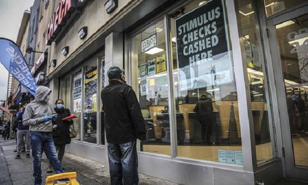 In this April 24, 2020, photo, people maintain social distancing and wear face masks due to COVID-19 concerns, while waiting to enter a check cashing service center in the Brooklyn borough of New York. While millions of U.S. workers have already received a quick relief payment from the federal treasury through direct deposit, millions of others without traditional bank accounts must wait weeks for paper checks. Advocates for the poor say this is an opportunity to get many of those who are unbanked into the formal financial system. (AP Photo/Bebeto Matthews)