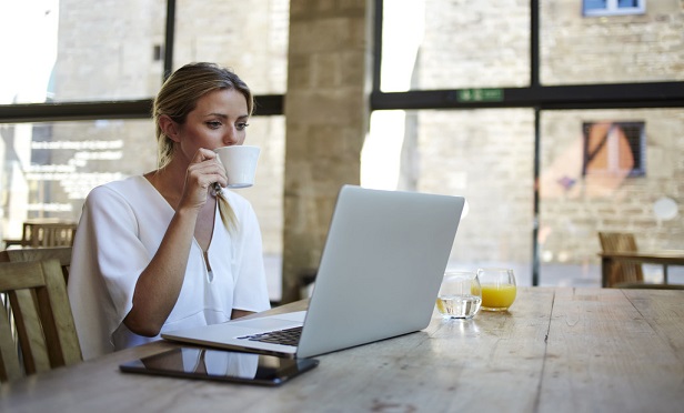 Young woman drinking coffee in front of her computer at home.