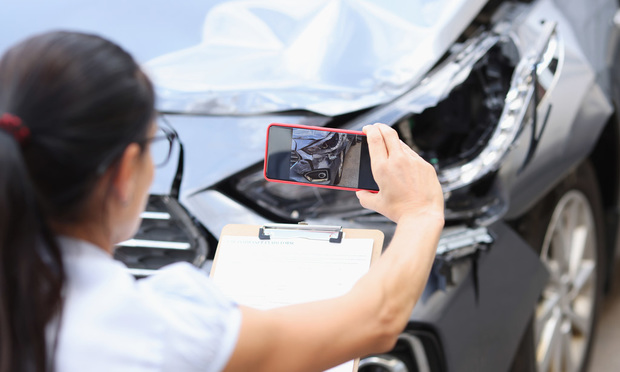Insurance agent taking a cell phone photo of a car after an accident.