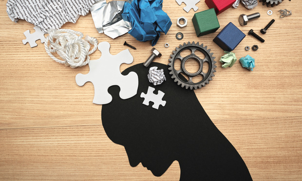 A dark silhouette of a head looks down as various items, including gears and puzzle pieces are coming out of the head. 