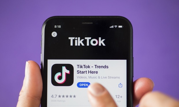 A person interacts with a mobile phone displaying the TikTok app.