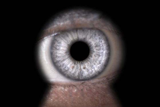 A close-up shot of an eye with a gray iris looking through a keyhole.