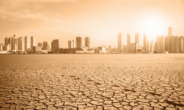 A city skyline sits behind a stretch of dry, barren land.