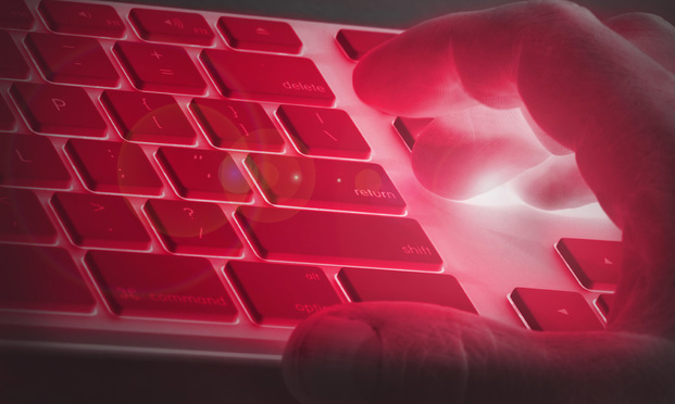 A hand hovers over a keyboard as both are illuminated by a red light.