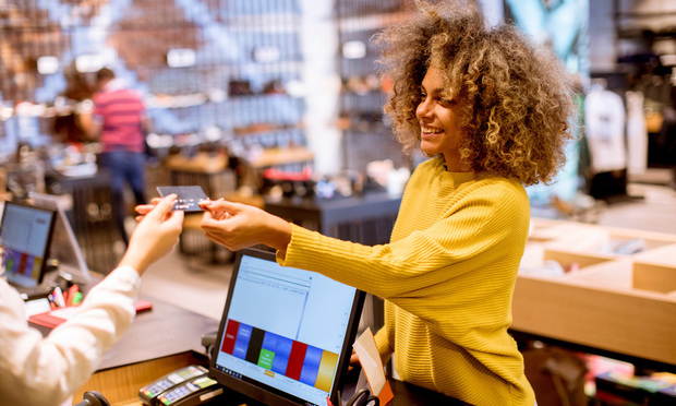 A woman hands her credit card to the person at the cash register in a store.