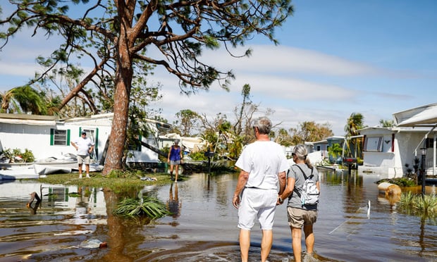 People walk on a flooded street at a trailer park following Hurricane Ian in Fort Myers, Florida, US, on Thursday, Sept. 29, 2022.
