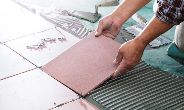 A person's hands are shown as they install a tile floor.