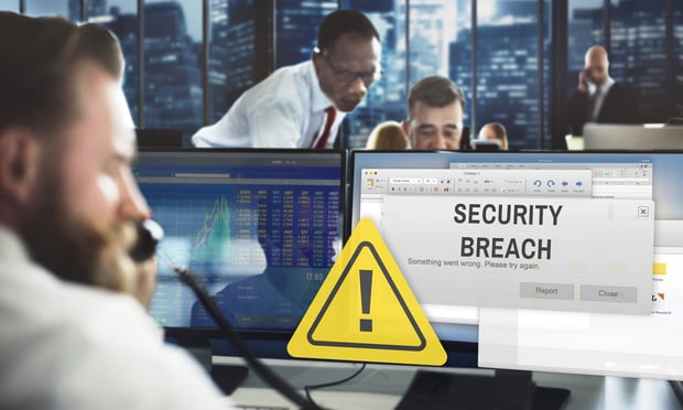 A man holds a phone to his ear as he sits in his office with a large "security breach" alert on his computer screen.