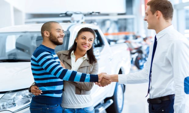 A couple shake hands with a salesman at a car dealership.