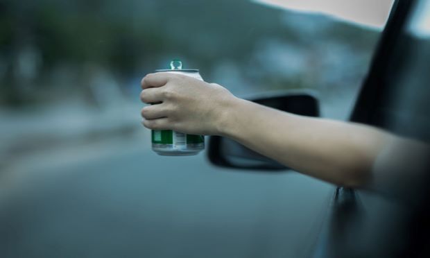 A person holds a drink out of their car window as they drive.