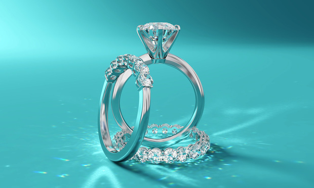 Two wedding bands and an engagement ring stand against a Tiffany-blue background.