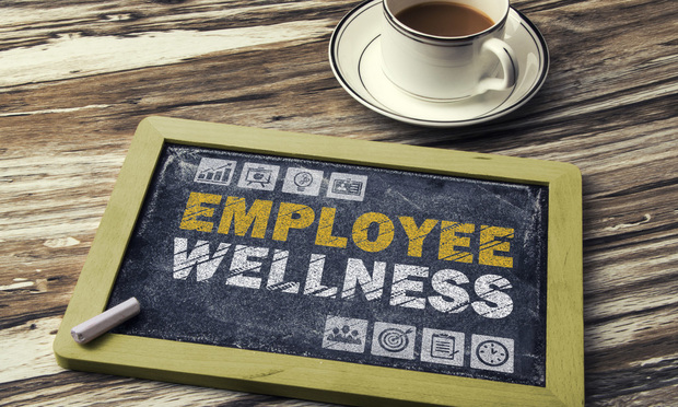 A chalkboard that says "employee wellness" lays on the ground next to a cup of coffee.