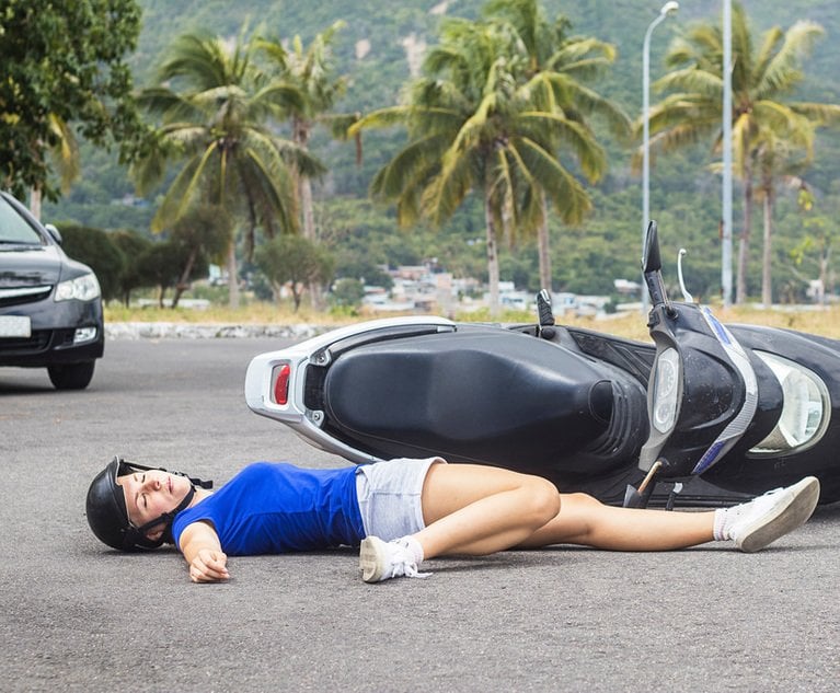 A woman lays on the road next to an overturned moped.