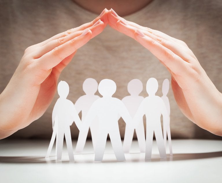 A person holds their hands in a roof shape over a group of paper people, as though to protect them.
