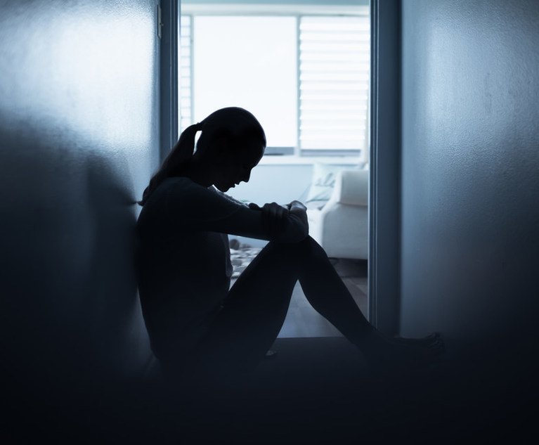 A person sits somberly at the end of a dark hallway